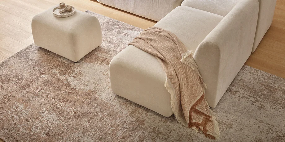 Jasna sofa z wygodnym siedziskiem, ozdobiona tekstyliami w naturalnych kolorach, ustawiona na dywanie.